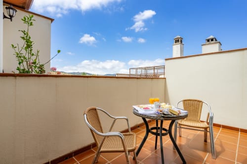 Terrasse ensoleillée de l'Hôtel Balcón De Los Montés avec fauteuils en rotin, table, vue montagne et paysage de Colmenar