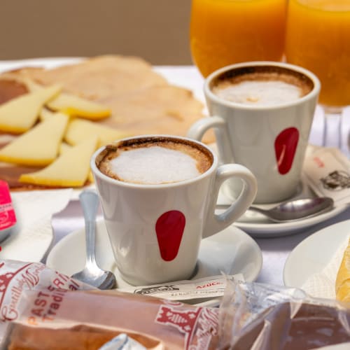 Deux cappuccinos décorés de cœurs, tranches de fromage, jus d'orange et viennoiseries sur table blanche à l'Hotel Balcón De Los Montés