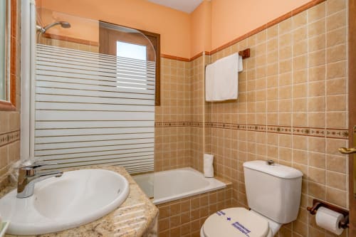 Salle de bain moderne de la suite Hotel Balcón De Los Montés avec carrelage beige, douche vitrée, lavabo et toilettes à Colmenar, Espagne