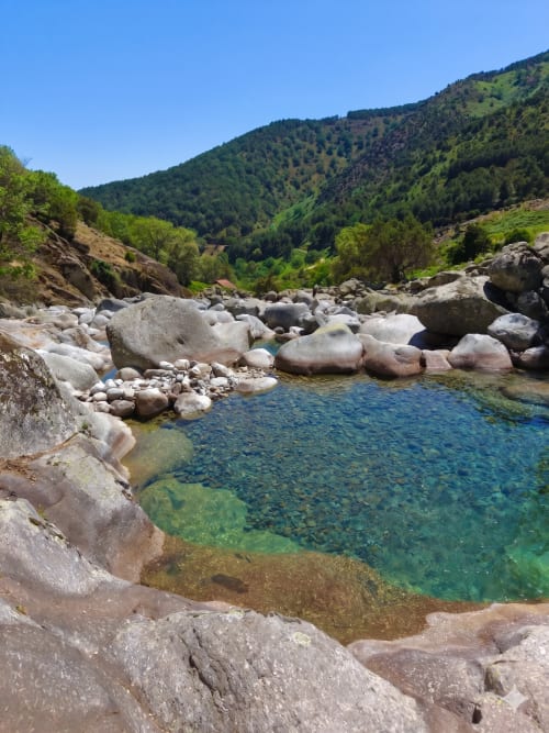 Arroyo de montaña cristalino con rocas rodeado de colinas boscosas cerca de Candeleda