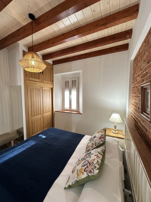 Acogedor dormitorio en El Escondite De Pedro Malillo en Candeleda con vigas expuestas, pared de ladrillo y lámpara colgante tejida