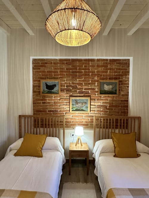 Habitación doble con pared de ladrillo visto, obra de arte de aves de corral, camas de madera con almohadas mostaza en El Escondite De Pedro Malillo