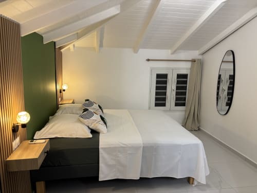 Modern bedroom in Gîte Cythère cottage at Domaine De Marly, Sainte-Anne with queen bed, green accent wall, and garden view
