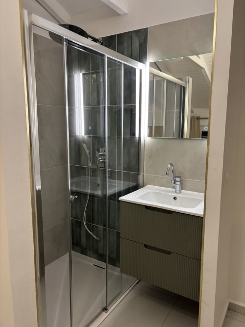 Modern bathroom in Gîte Cythère cottage at Domaine De Marly with glass shower enclosure, white sink, and mirror lighting