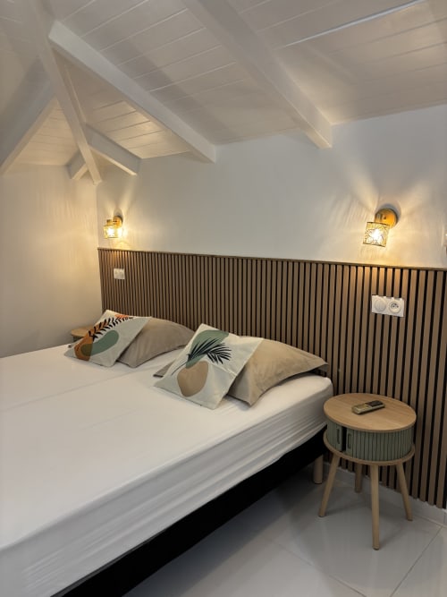 Modern bedroom in Gîte Cythère cottage at Domaine De Marly with white walls, exposed beams, striped headboard, and garden