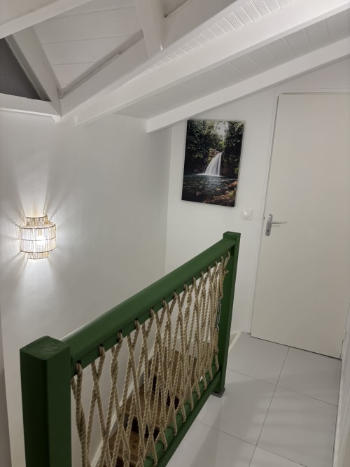 Modern cottage hallway with green rope railing, waterfall artwork, and pendant lighting at Domaine De Marly, Sainte-Anne