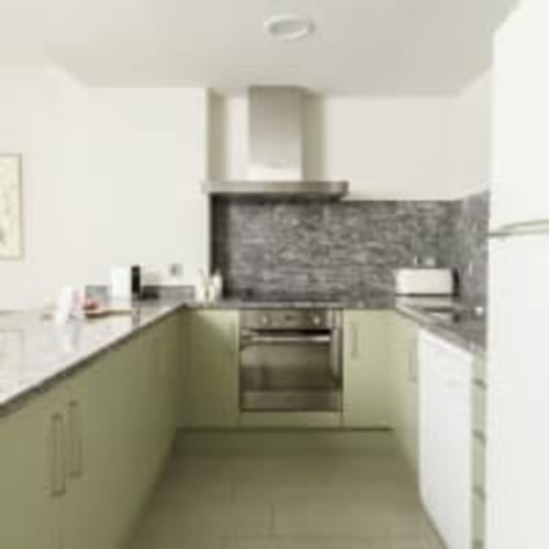 Cocina moderna en el apartamento Racons de Vic con armarios verde pálido, horno de acero inoxidable y salpicadero oscuro