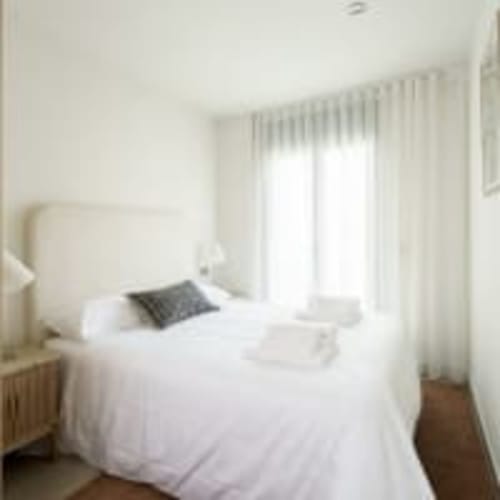 Dormitorio luminoso en el apartamento Racons en Vic con cama blanca, vistas a la ciudad y mobiliario moderno