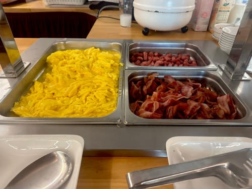Breakfast buffet at Verdi Hotel Jesolo: scrambled eggs, bacon strips, and diced ham in metal serving trays