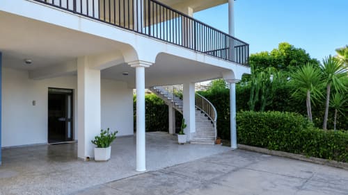 Terrazza di moderna villa a Noto con colonne bianche, vista sul giardino e scala curva verso il livello superiore