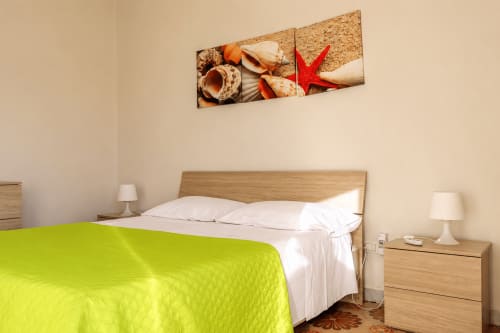 Camera luminosa a Villa Leuka San Lorenzo a Noto con biancheria verde lime, mobili in legno e decorazioni marine sopra il letto