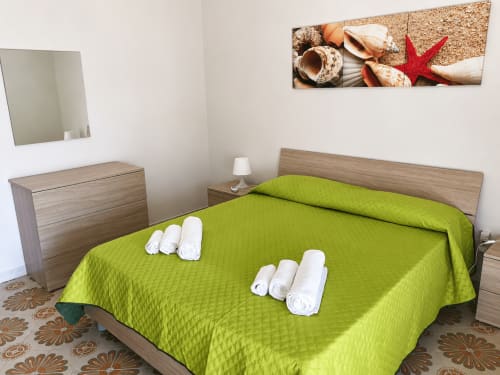 Copriletto verde acceso con asciugamani bianchi arrotolati nella camera della Villa Leuka San Lorenzo, hotel a Noto in Sicilia con dettagli in legno
