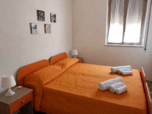 Camera da letto arancione luminosa con asciugamani bianchi ordinatamente disposti sul letto a Villa Leuka San Lorenzo a Noto, Italia