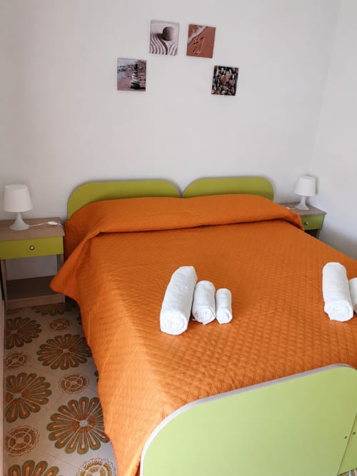 Camera vivace di Villa Leuka San Lorenzo a Noto con testata verde lime, biancheria arancione, asciugamani bianchi arrotolati