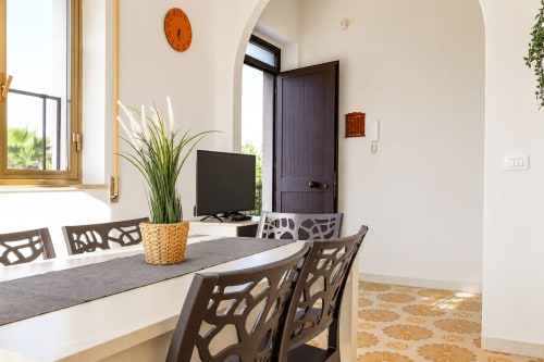 Zona pranzo moderna con sedie geometriche, pianta in vaso e porta scura nella villa di Noto