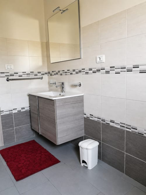 Bagno moderno di Villa Leuka San Lorenzo a Noto con piastrelle bianche, dettagli scuri, lavabo e tappeto rosso