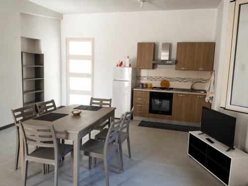 Zona pranzo e cucina della villa moderna a Le Terre di Ebe, Noto Sicilia con tavolo da pranzo, mobili in legno e zona TV