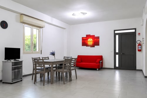 Soggiorno moderno a Le Terre di Ebe, Noto: divano rosso, tavolo da pranzo, TV, finestra con vista giardino, climatizzatore