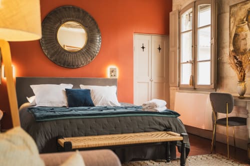 Chambre moderne aux Jardins de Baracane avec murs orange, lit noir, miroir rond et vue sur le jardin à Avignon