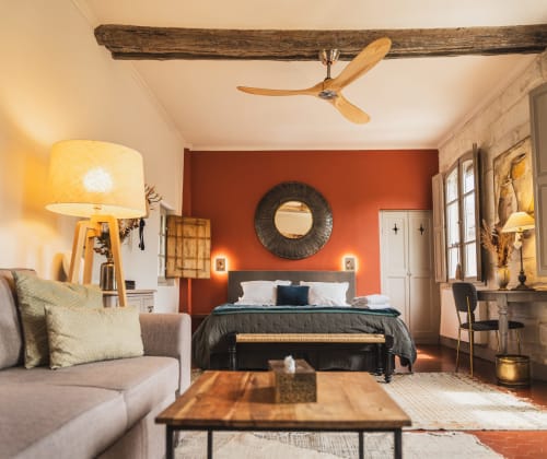 Chambre élégante aux Jardins de Baracane à Avignon avec poutres rustiques, mur d'accent orange et mobilier contemporain.