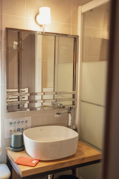 Lavabo moderne avec vasque blanche ronde, grand miroir et applique murale aux Jardins de Baracane à Avignon
