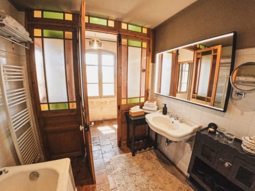 Salle de bain élégante avec portes en bois, double vasque et équipements vintage aux Jardins de Baracane à Avignon
