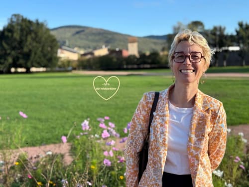 Femme souriante aux Gîtes les Orchidées à Cluny, France, avec champs verdoyants et fleurs violettes
