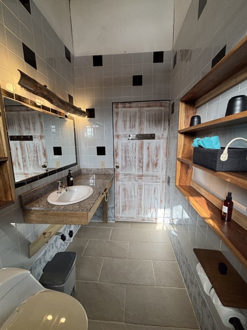 Modern bathroom at BarrBra BnB in Bocas del Toro with sink, toilet, walk-in shower, wooden shelving, and tiled walls