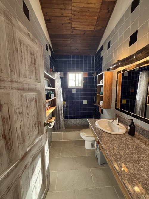 Modern bathroom at BarrBra BnB in Bocas del Toro with granite countertop, dark tile shower, and wooden accents