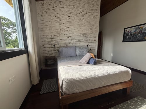 Queen bed with white bedding in bright BarrBra BnB room, Bocas del Toro, with sea view window and textured accent wall