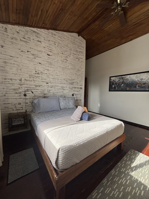 Queen bed with white mattress in BarrBra BnB room, Bocas del Toro, featuring wooden wall and AC unit