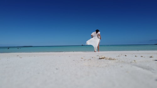 Femme en robe blanche sur la plage de sable blanc pristine de Belamandy Lodge, Nosy Be avec eaux océan turquoise