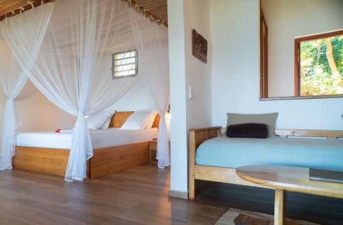 Chambre spacieuse de la villa Belamandy Lodge à Nosy Be avec lit à baldaquin, mobilier en bois et vue sur mer