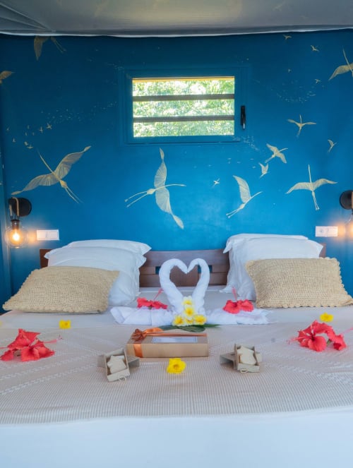 Chambre romantique de la villa en bord de mer de Belamandy Lodge, Nosy Be, avec murs bleus, fresque d'oiseau volant et vue sur l'océan.