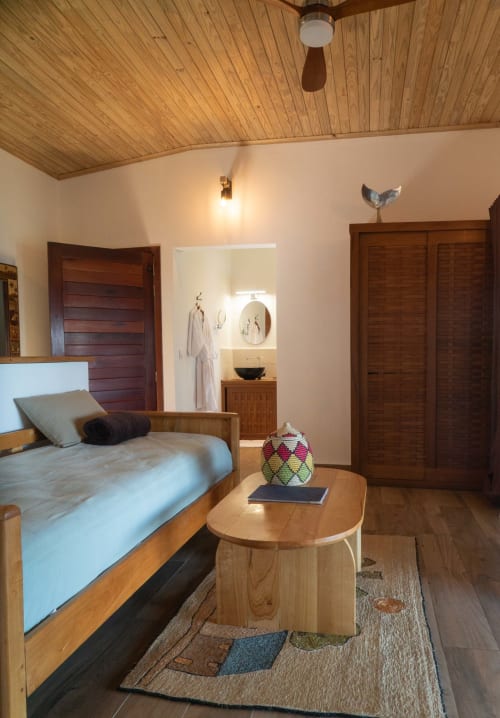 Chambre de la villa Belamandy Lodge avec ventilateur en bois, vue sur mer, lit garni, table en bois et entrée de salle de bains