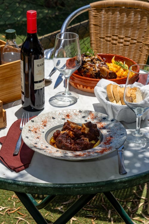 Refeição ao ar livre no Hotel Balcón De Los Montés com vinho tinto espanhol, prato de carne, pão e vegetais grelhados