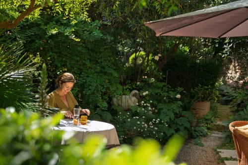 Femme se relaxant dans la cour fleurie des Jardins de Baracane à Avignon avec parasol et boissons