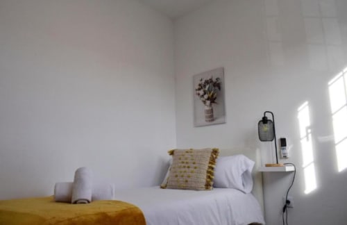 Dormitorio luminoso en Gestyp-AT Mérida con sábanas blancas, almohadas amarillas y luz natural de ventanas