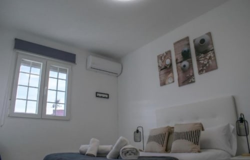 Moderno dormitorio en Gestyp-AT Mérida con paredes blancas, cama con almohadas, aire acondicionado y vista a la ciudad