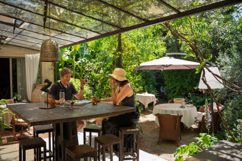 Deux clients dînent sur la terrasse des Jardins de Baracane à Avignon, entourés de verdure luxuriante et d'ombre de pergola