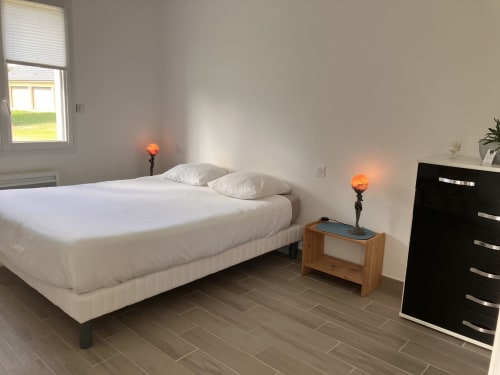 Chambre moderne du gîte Domaine Des Bois Argentés avec lit blanc, table de nuit en bois, lampes orange et vue sur le jardin