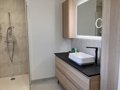 Salle de bain moderne avec lavabo blanc, plan de travail noir, miroir LED et douche à l'italienne à la Maison des Bois Argentés
