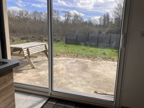 Vue du jardin champêtre du Domaine Des Bois Argentés avec banc en bois, terrasse et paysage boisé au-delà de la clôture