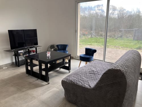Salon moderne du gîte avec canapé gris, table basse noire, téléviseur et vue sur le jardin