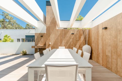 Terraço de jantar de villa moderna com mesa, cadeiras brancas, paredes de madeira e céu azul em Aroeira, Portugal