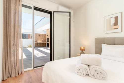 Quarto moderno com roupa de cama branca, cabeceira cinza e portas deslizantes para o terraço na villa Republica do Sul em Portugal