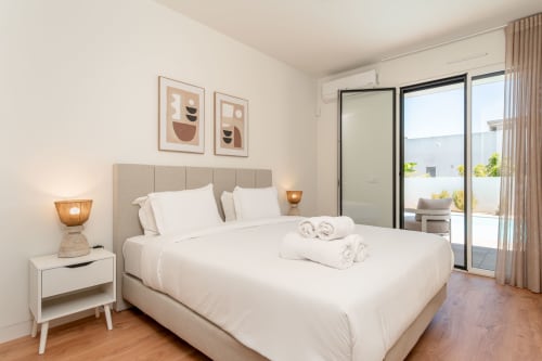 Quarto de villa moderna na Republica do Sul com cabeceira bege, roupas de cama brancas, portas para terraço e decoração minimalista em Charneca