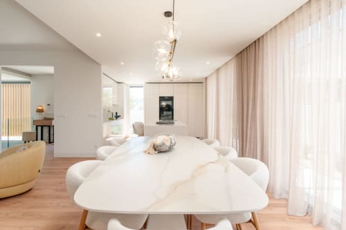 Sala de jantar de villa moderna com mesa de mármore, cadeiras brancas, iluminação pendente e cortinas translúcidas em Aroeira, Portugal
