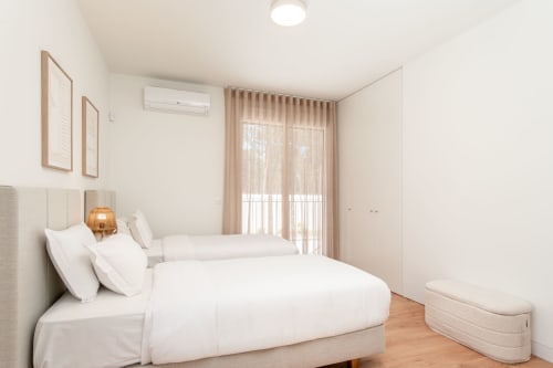 Quarto de villa moderna com camas de solteiro, roupas de cama brancas, piso de madeira e acesso por porta de vidro à varanda na Quinta do Pinhão,