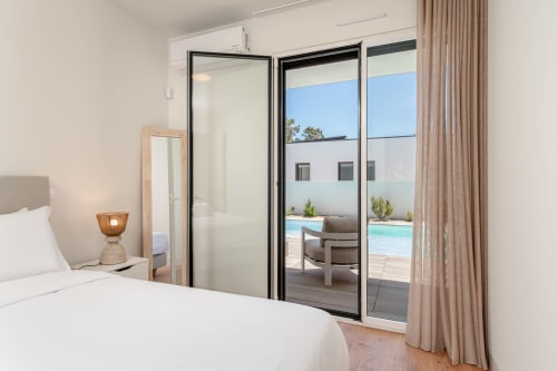 Modern bedroom in Charneca da Caparica villa with sliding glass doors opening to pool and sea views, neutral décor with white
